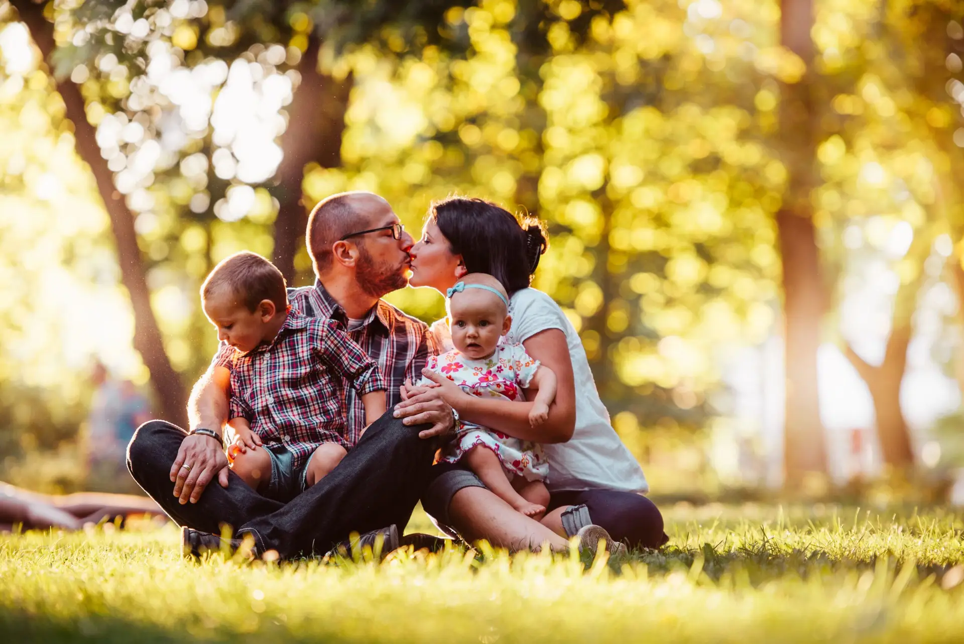 Family of four enjoying a sunny day outdoors, capturing a loving moment in nature.
